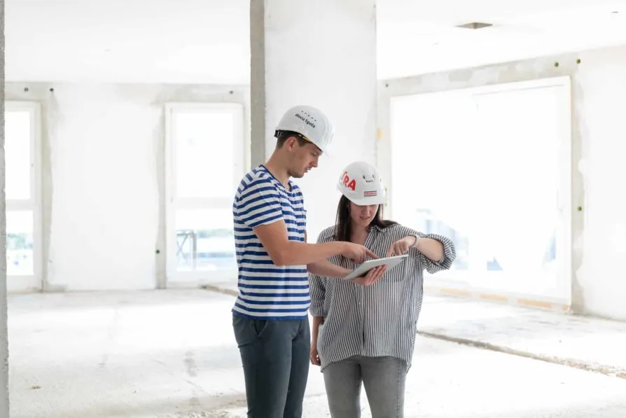 Zwei Projektbeteiligte stimmen sich auf der Baustelle mit einem Tablet ab und prüfen digitale Bauinformationen gemeinsam vor Ort.“